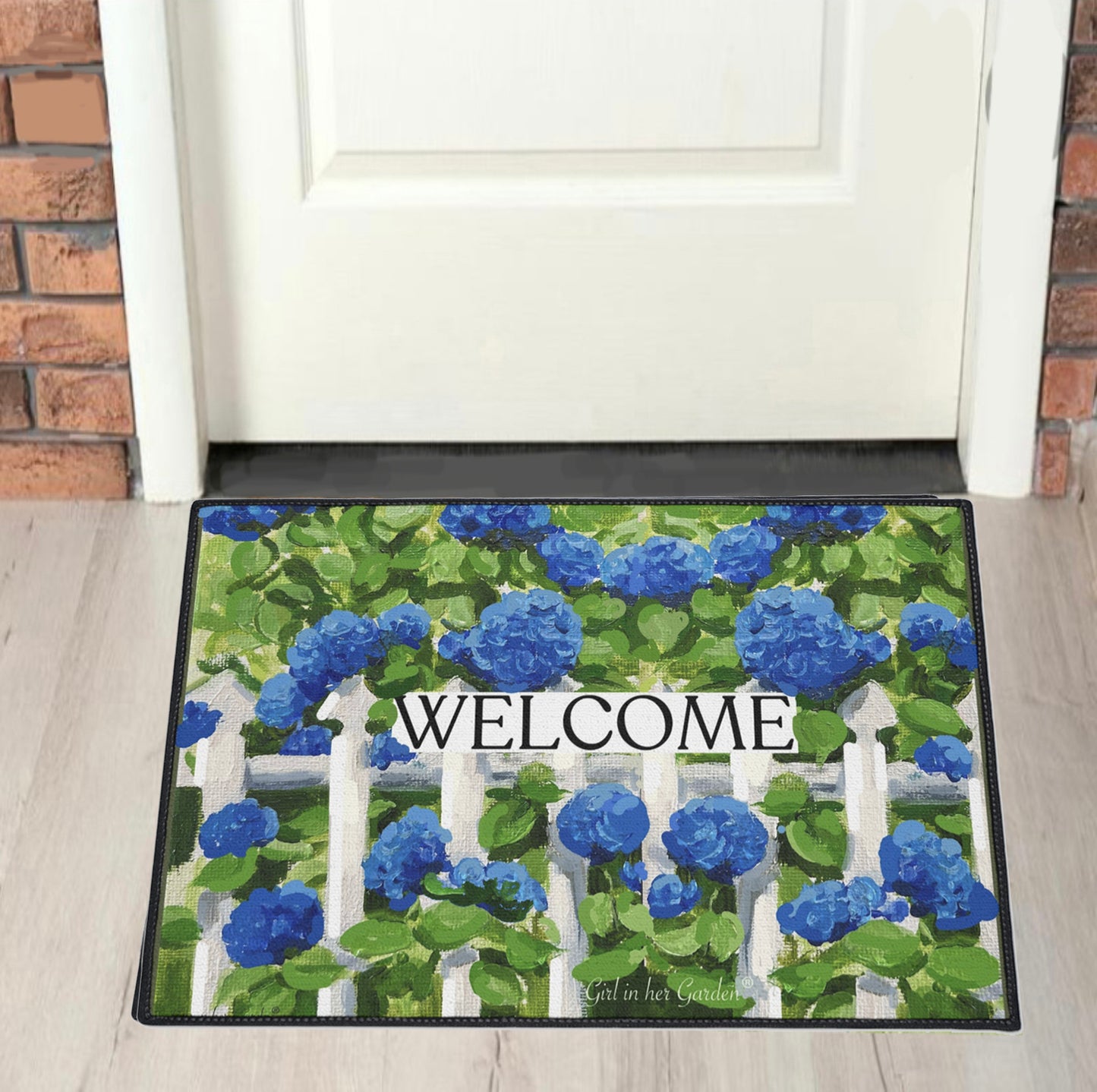 Decorative doormat with blue flowers and 'Welcome' text on a wooden floor.