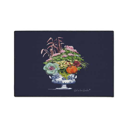 A rectangular navy blue mat or placemat featuring a central watercolor-style illustration of a floral arrangement in a blue-and-white pedestal bowl, with the text 'Gold in Her Garden' printed near the bottom right of the design.