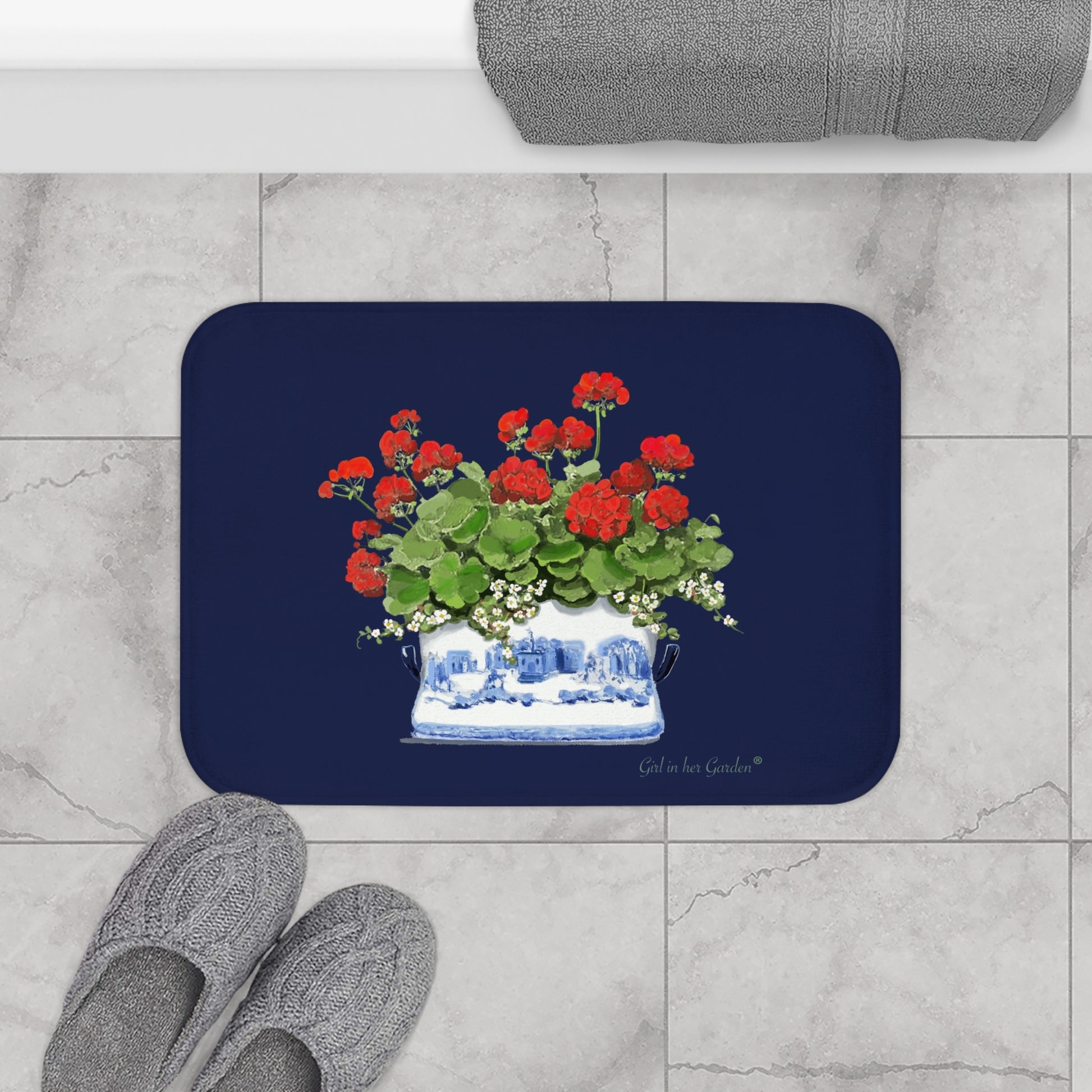 Navy bath mat with floral design on a marble floor with slippers.