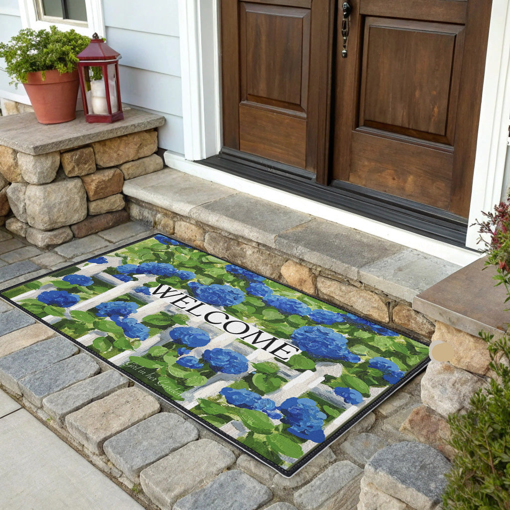 Decorative doormat with blue flowers and 'Welcome' text on a stone porch.