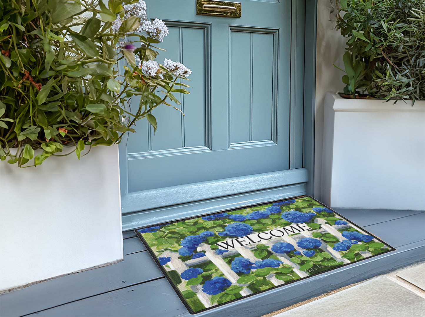 Decorative doormat with floral pattern and 'Welcome' text in front of a blue door.