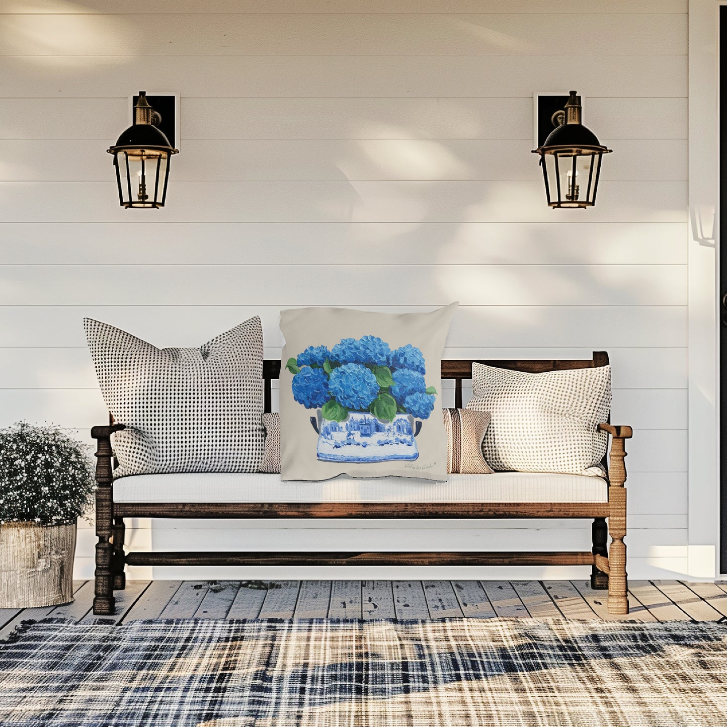 Wooden bench with decorative pillows on a porch with plaid rug and wall lights.