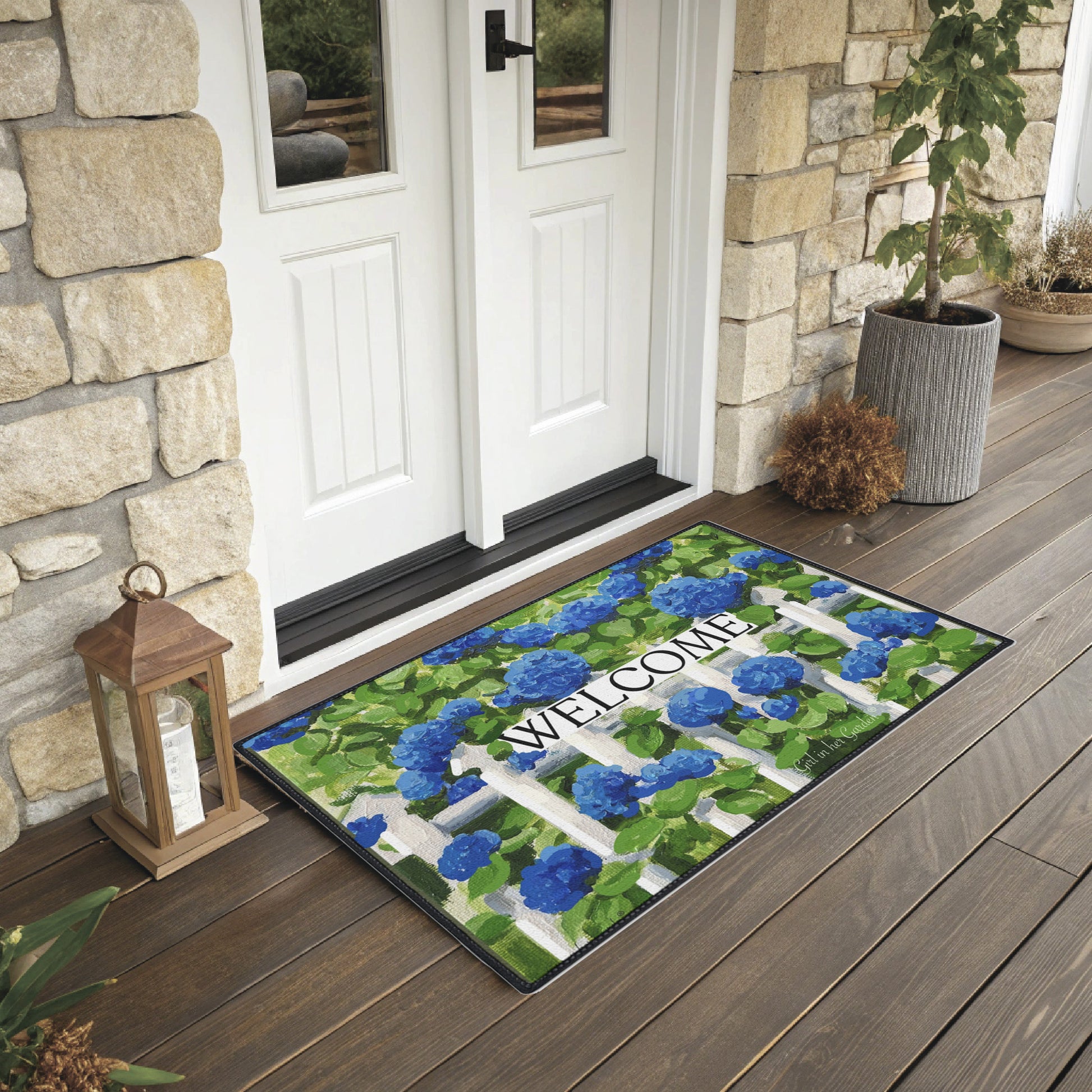 Decorative doormat with floral design and 'Welcome' text on a wooden porch.