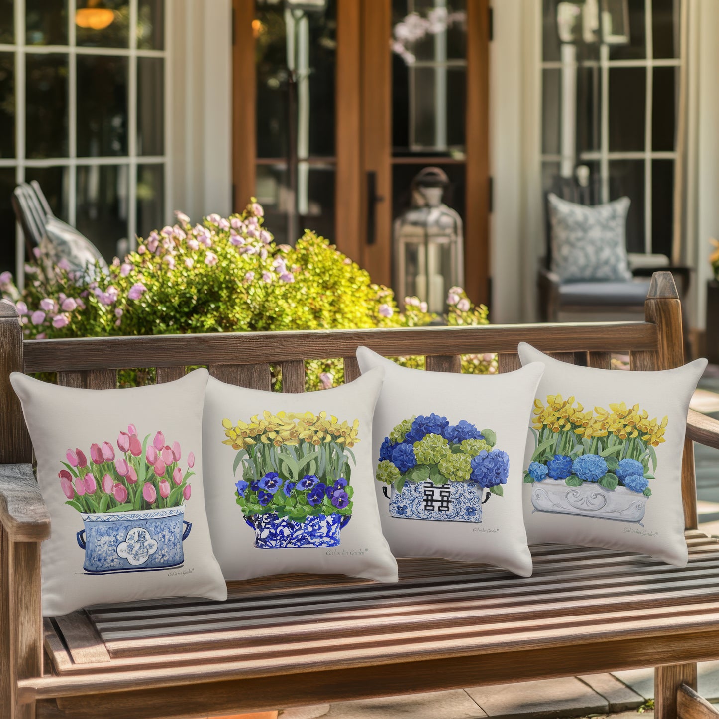 Four decorative pillows with floral designs on a wooden bench outdoors.