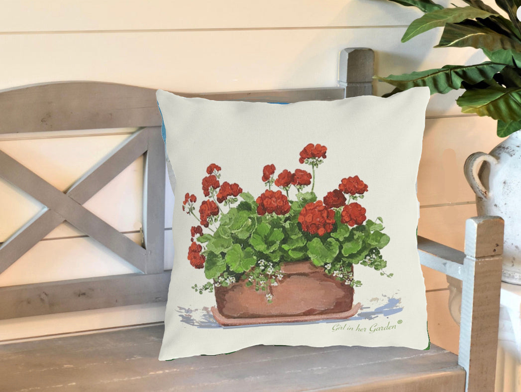 Decorative pillow with red geraniums on a wooden bench.