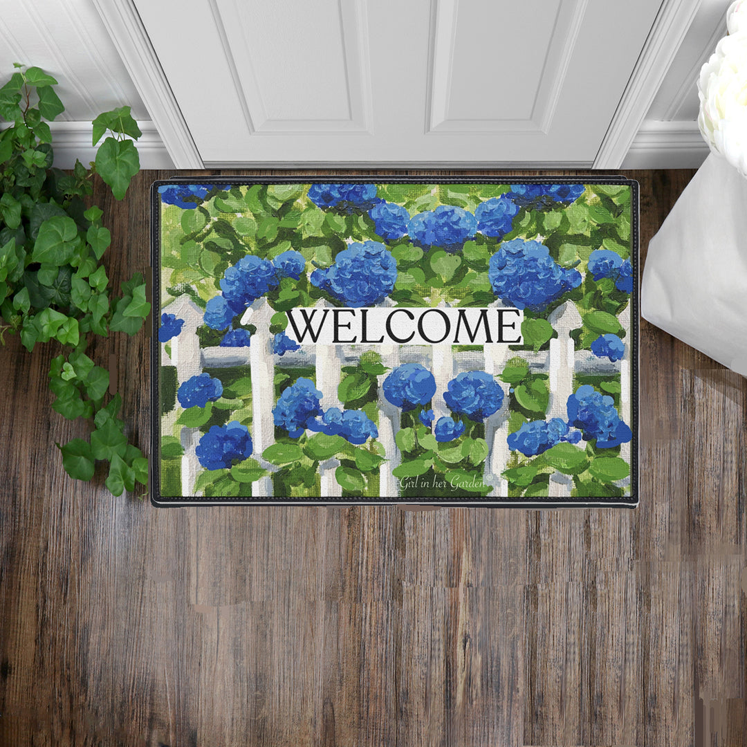 Decorative doormat with blue flowers and 'WELCOME' text on a wooden floor.